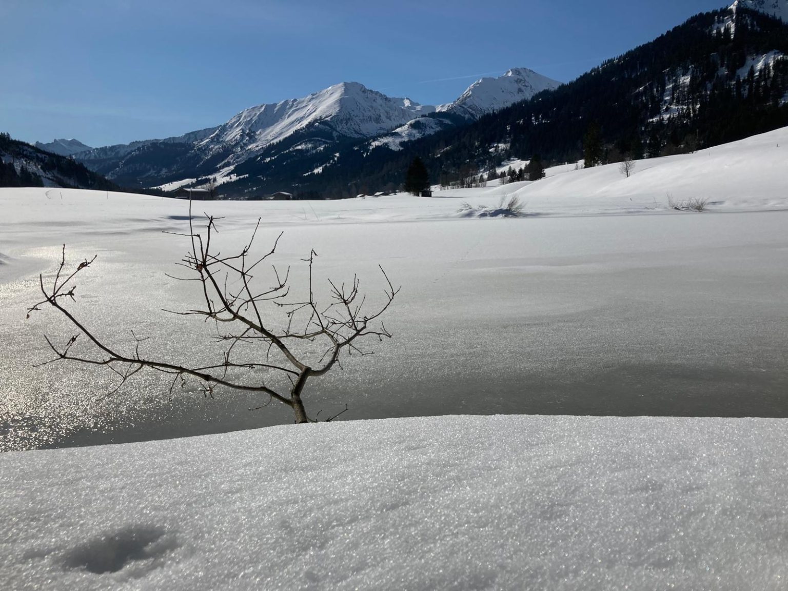 Zugefrorener See vor verschneiten Bergen